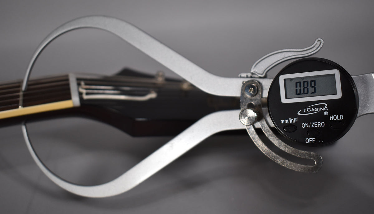A digital caliper measures the dark walnut neck of the guitar, displaying "0.89" on its screen.
