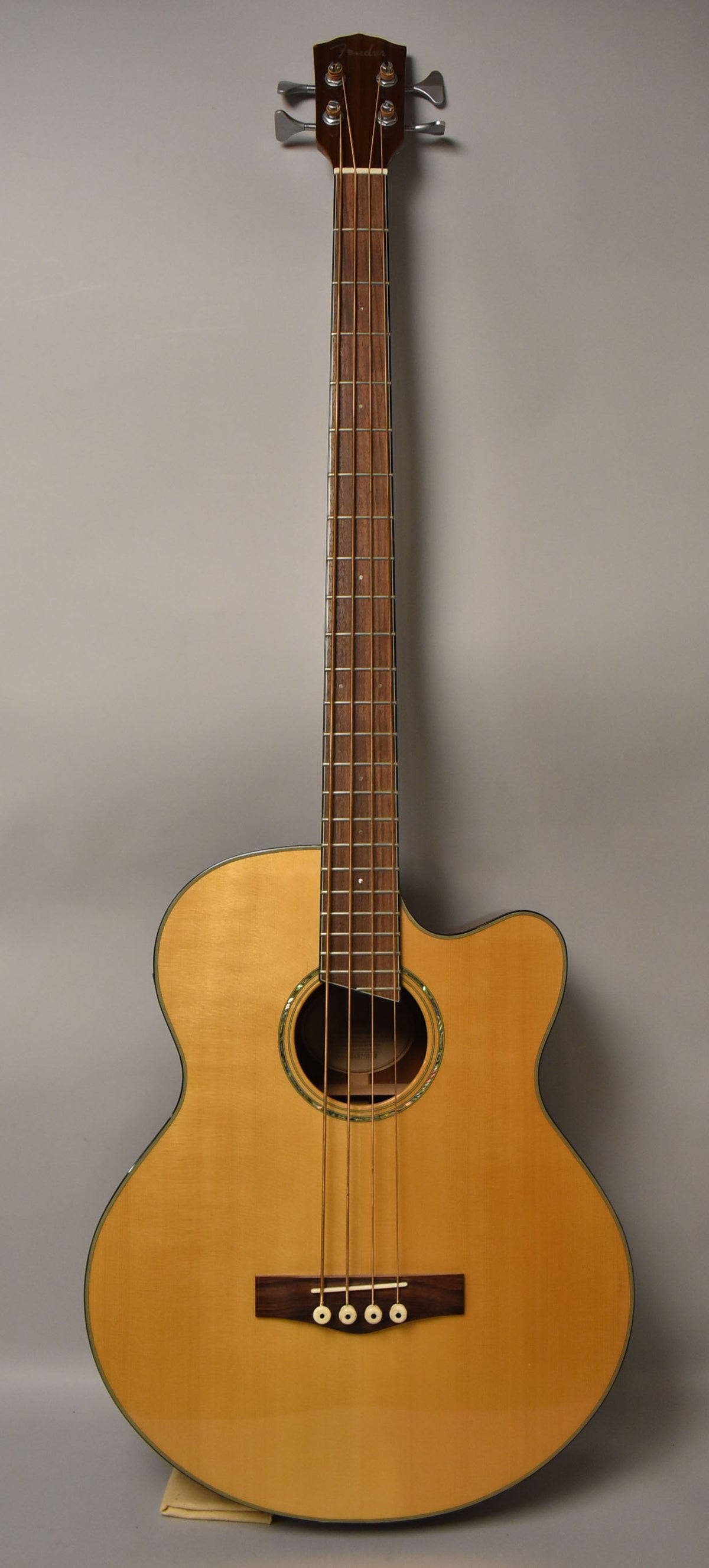Full front view of a natural finish acoustic bass with a cutaway, dark wood fingerboard, and a dark wood bridge with white pins.