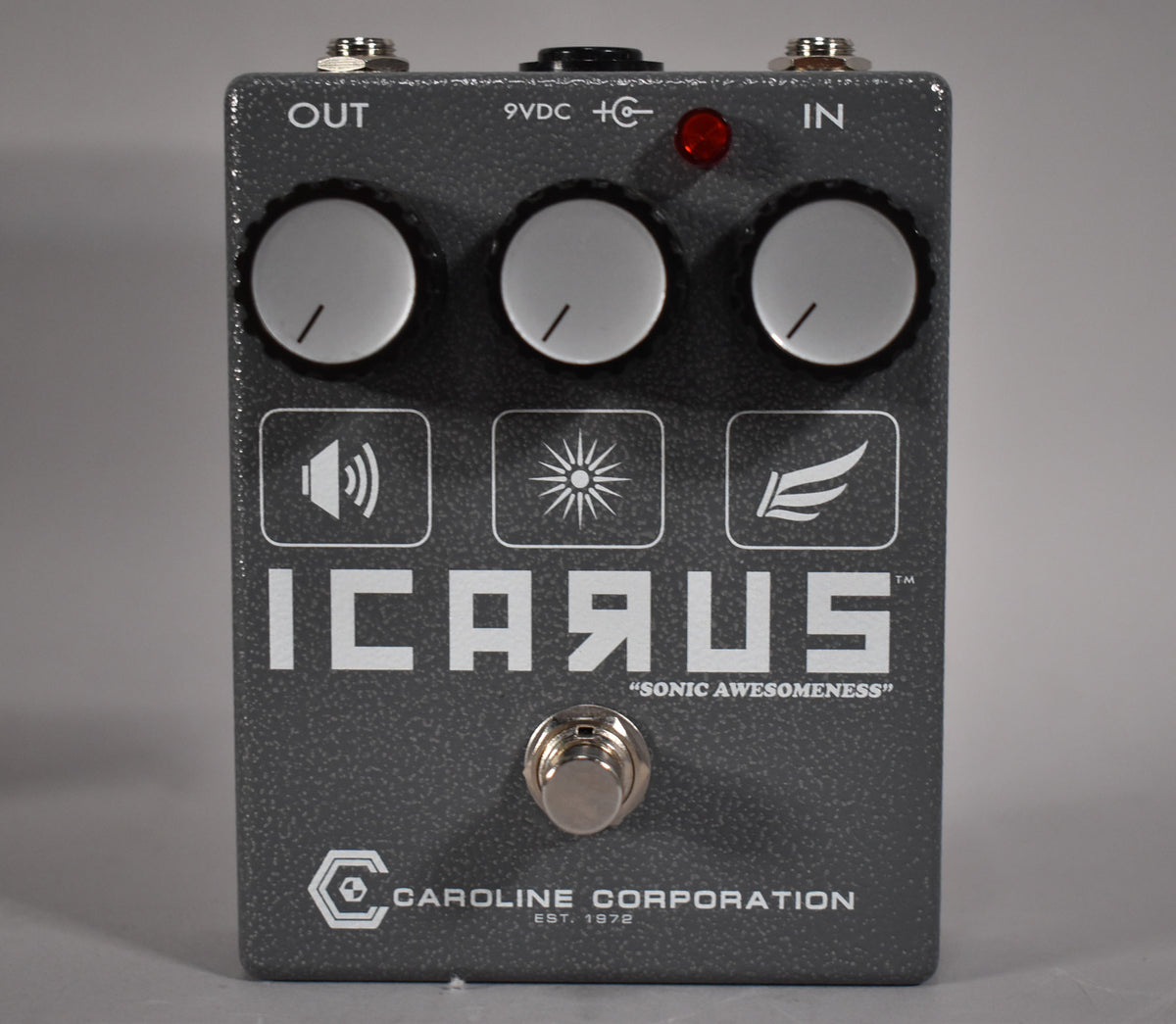 A dark gray textured pedal with three white knobs, a red LED, and a silver footswitch, viewed from the front.
