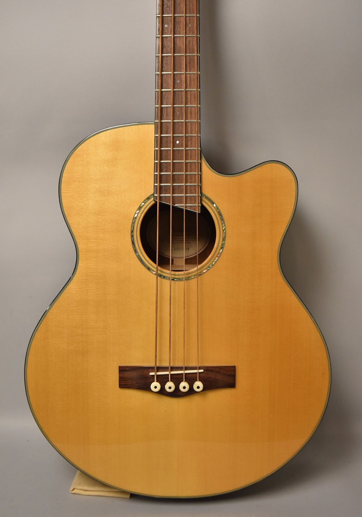 Full-front view of a natural finish acoustic bass with a cutaway, dark wood bridge, and abalone rosette.