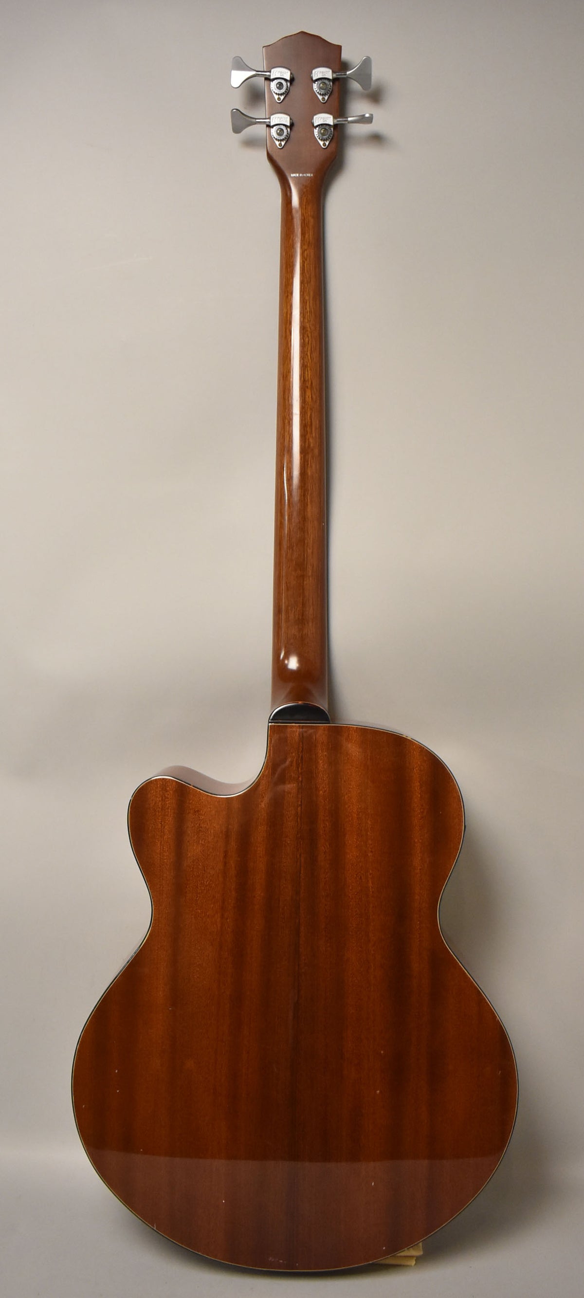 The acoustic bass is shown from the back, displaying a dark brown body and neck with a glossy finish and four chrome tuners.
