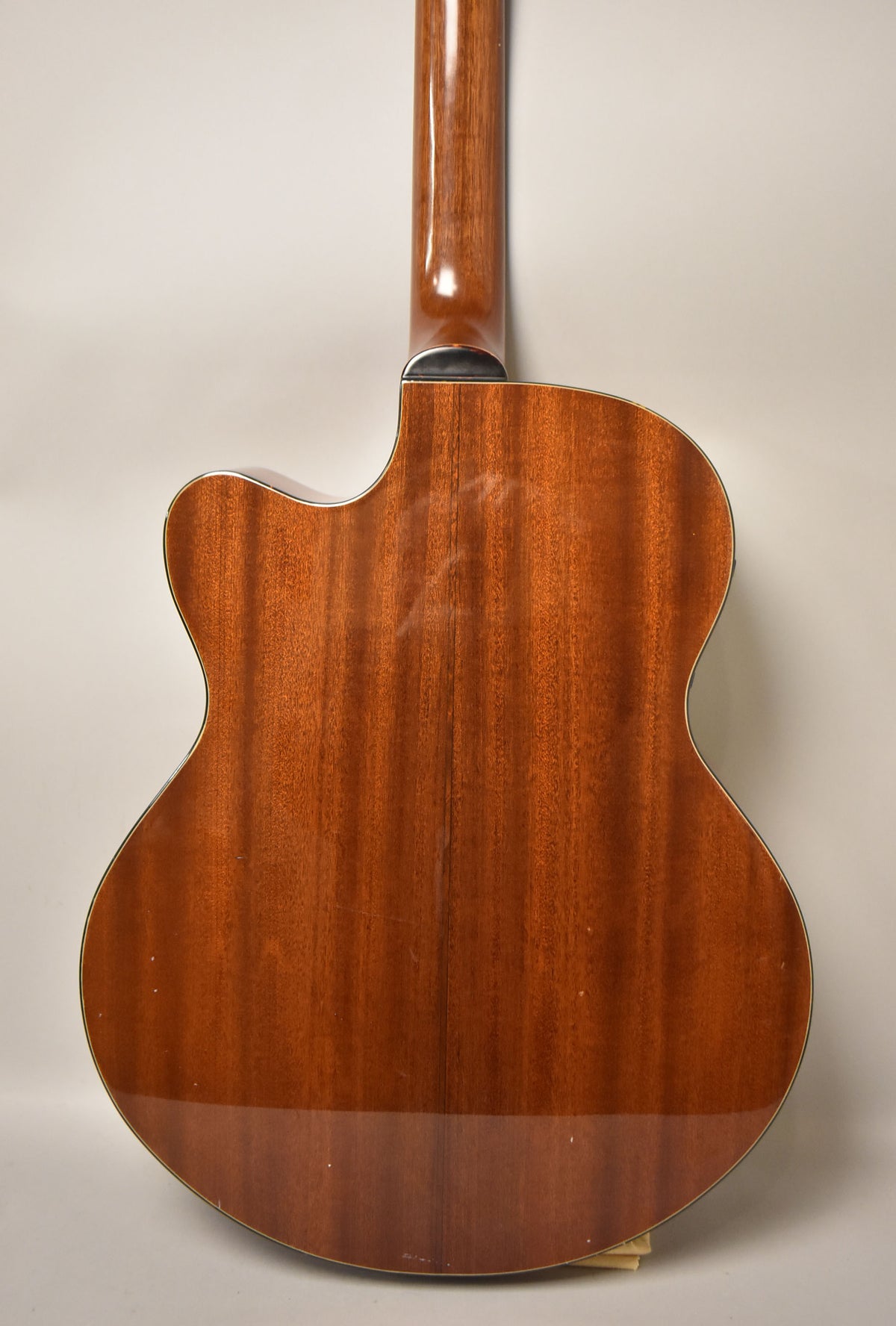 The acoustic bass's natural wood back and neck are shown, with a cutaway and visible light scratches on the body.