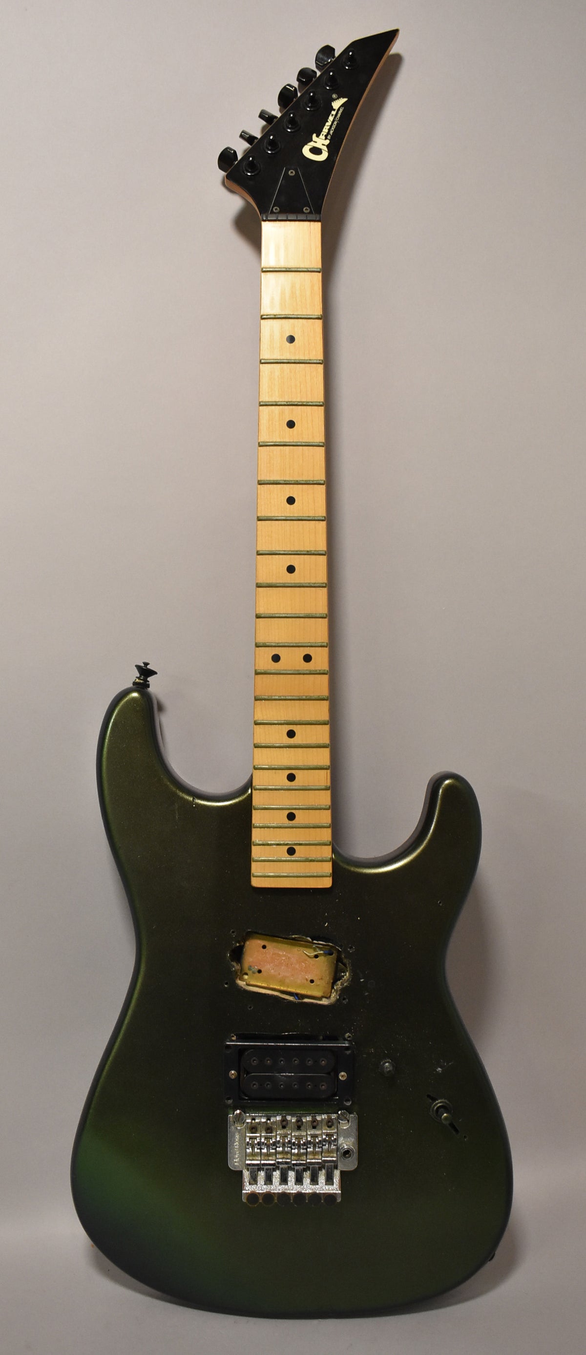 Full-length view of a dark green metallic electric guitar with a maple neck, black headstock, a single humbucker, and a Floyd Rose bridge.