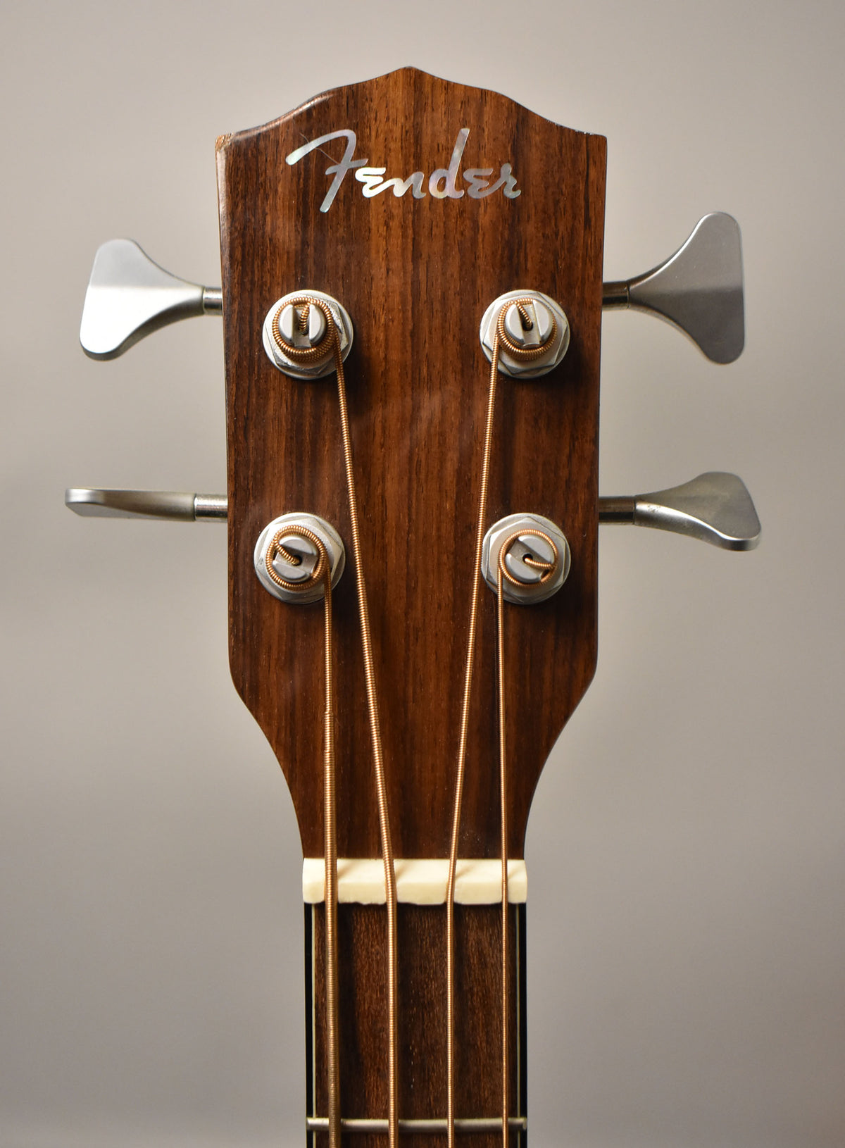 Close-up of the dark wood headstock with a chipped top edge, showing four silver tuners, bronze strings, and a white nut.