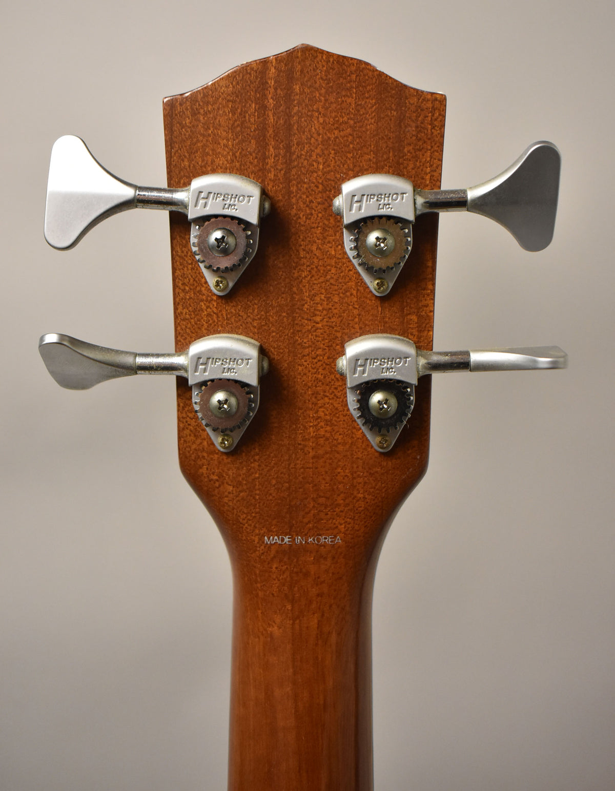 Rear view of the headstock and upper neck, showing four silver tuning machines with exposed gears on a natural wood finish.