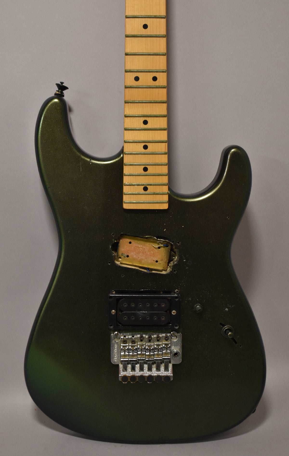 A dark green metallic guitar body with a maple neck, a single humbucker, a Floyd Rose bridge, and an empty middle pickup cavity.