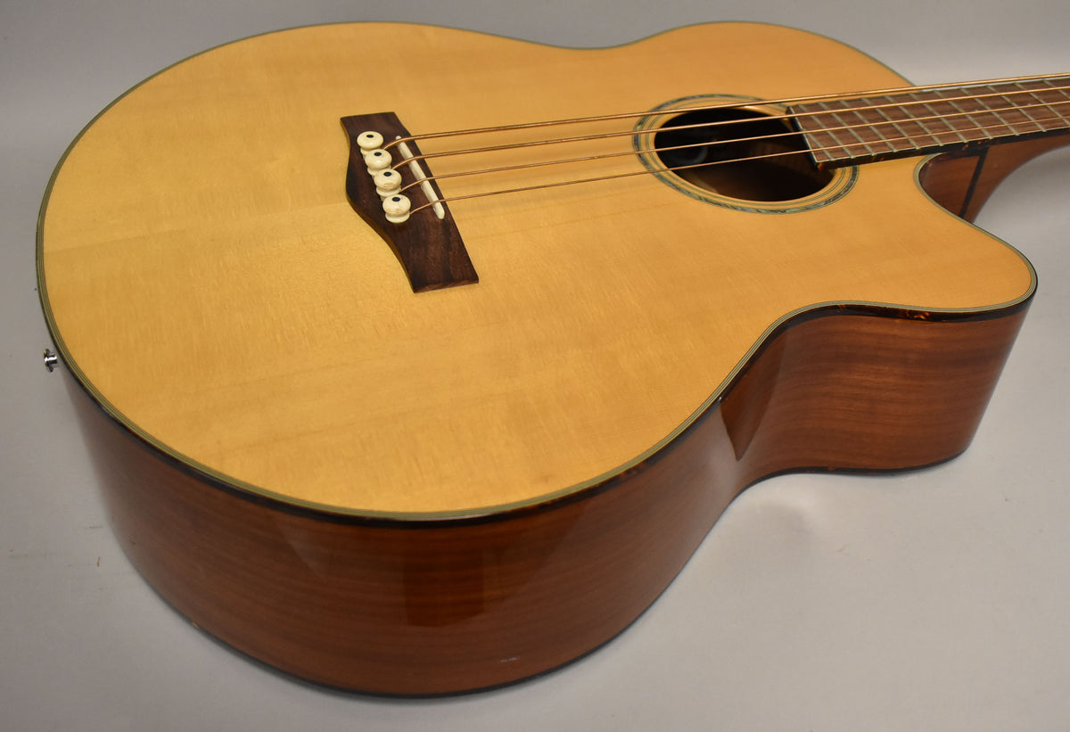 The natural finish acoustic bass is angled to show its light wood top, dark wood bridge with white pins, and glossy reddish-brown sides.