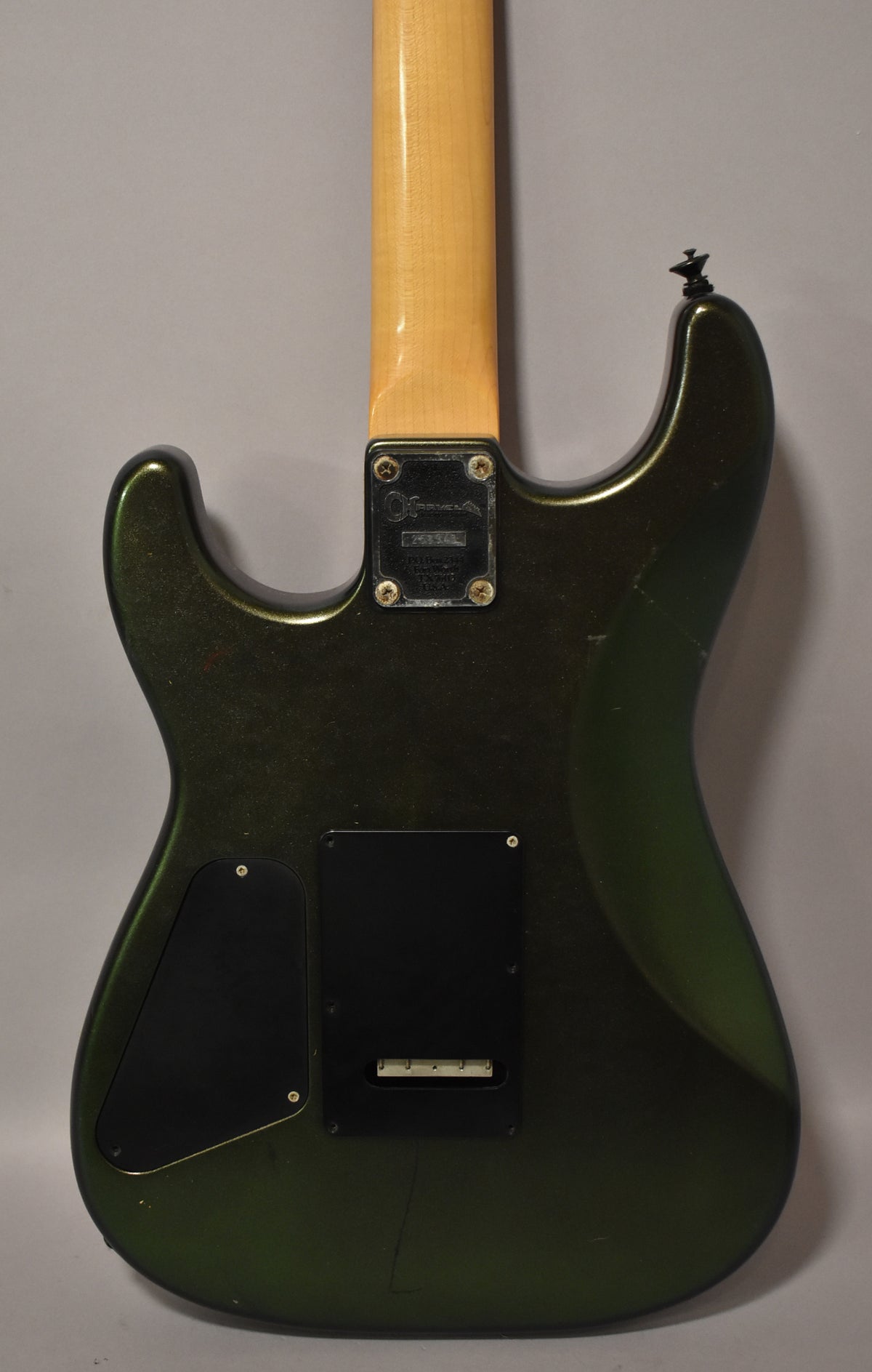 Rear view of a dark green metallic guitar body with a maple neck, showing two black control plates and finish wear.