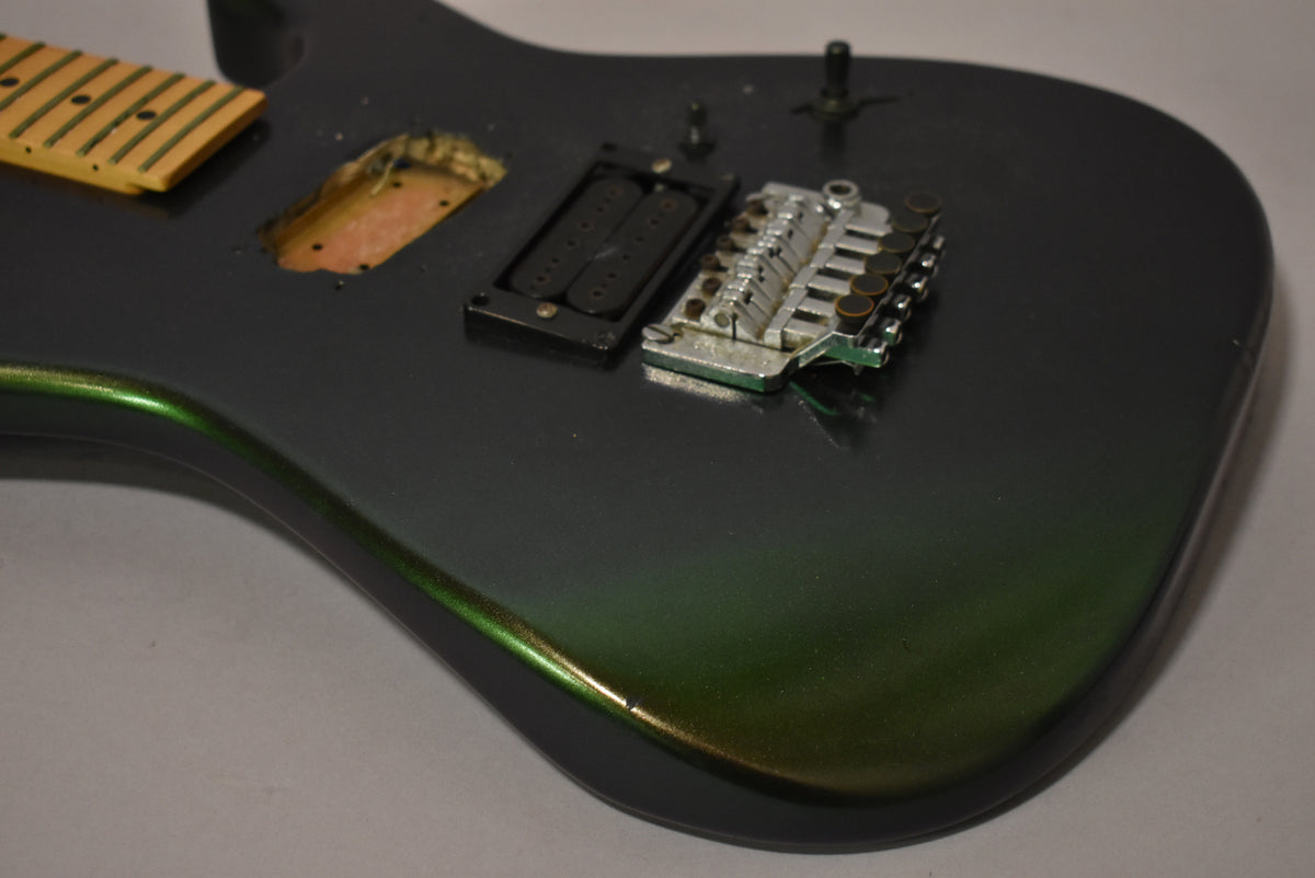 The dark metallic green guitar body, missing its neck, shows a pickup cavity, a black humbucker, and a worn chrome tremolo bridge.