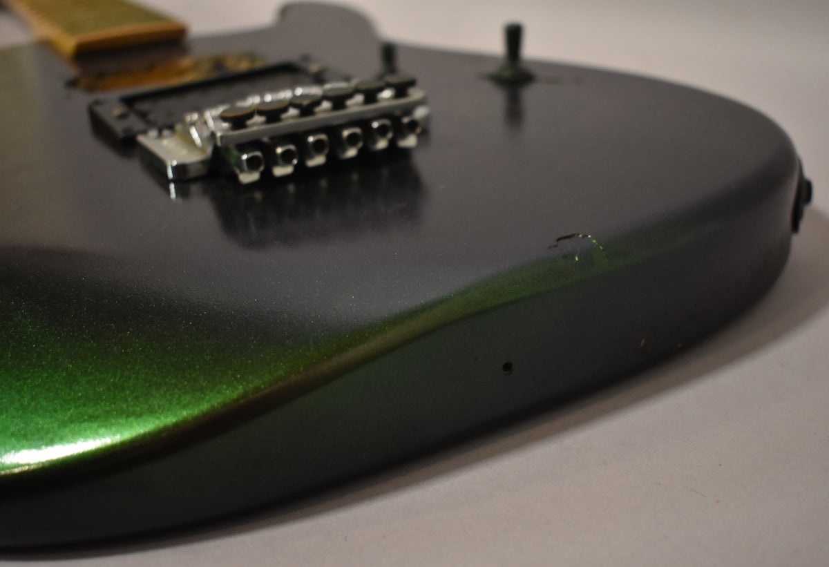 Close-up of the guitar body's lower bout, showing the metallic green finish, chrome tremolo, and a chip in the finish.