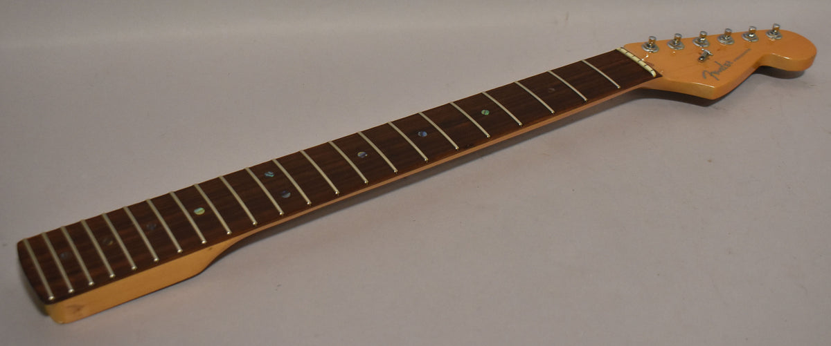 A Stratocaster neck, angled from the lower bout to the headstock, showing a dark fretboard with pearloid dots and six chrome tuners.