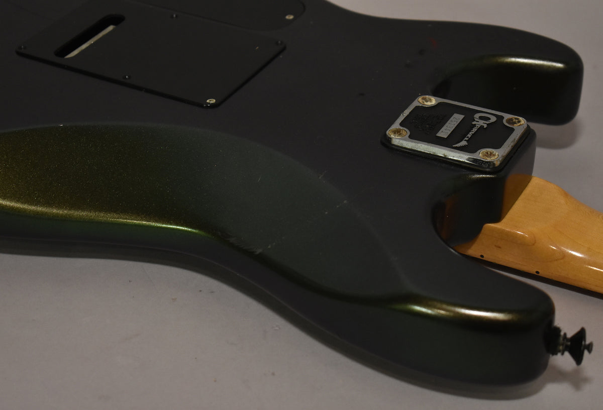 The guitar's dark green metallic body, viewed from the back, shows a worn neck plate, a black tremolo cover, and a maple neck joint.