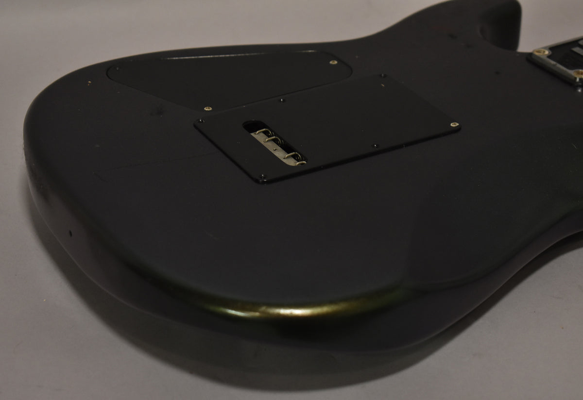 The back of a dark gray guitar body, showing a black tremolo cavity cover and wear along the lower edge.