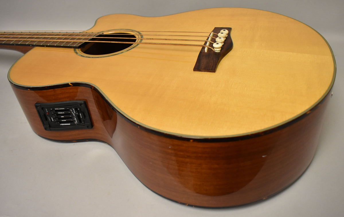 The natural finish acoustic bass is angled to show its light wood top, dark wood sides, and built-in preamp with EQ controls.