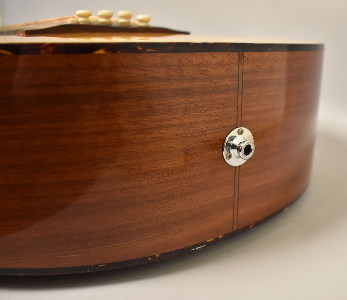 Close-up of the acoustic bass's lower bout, showing the natural wood grain, tortoiseshell binding, and a chrome output jack.