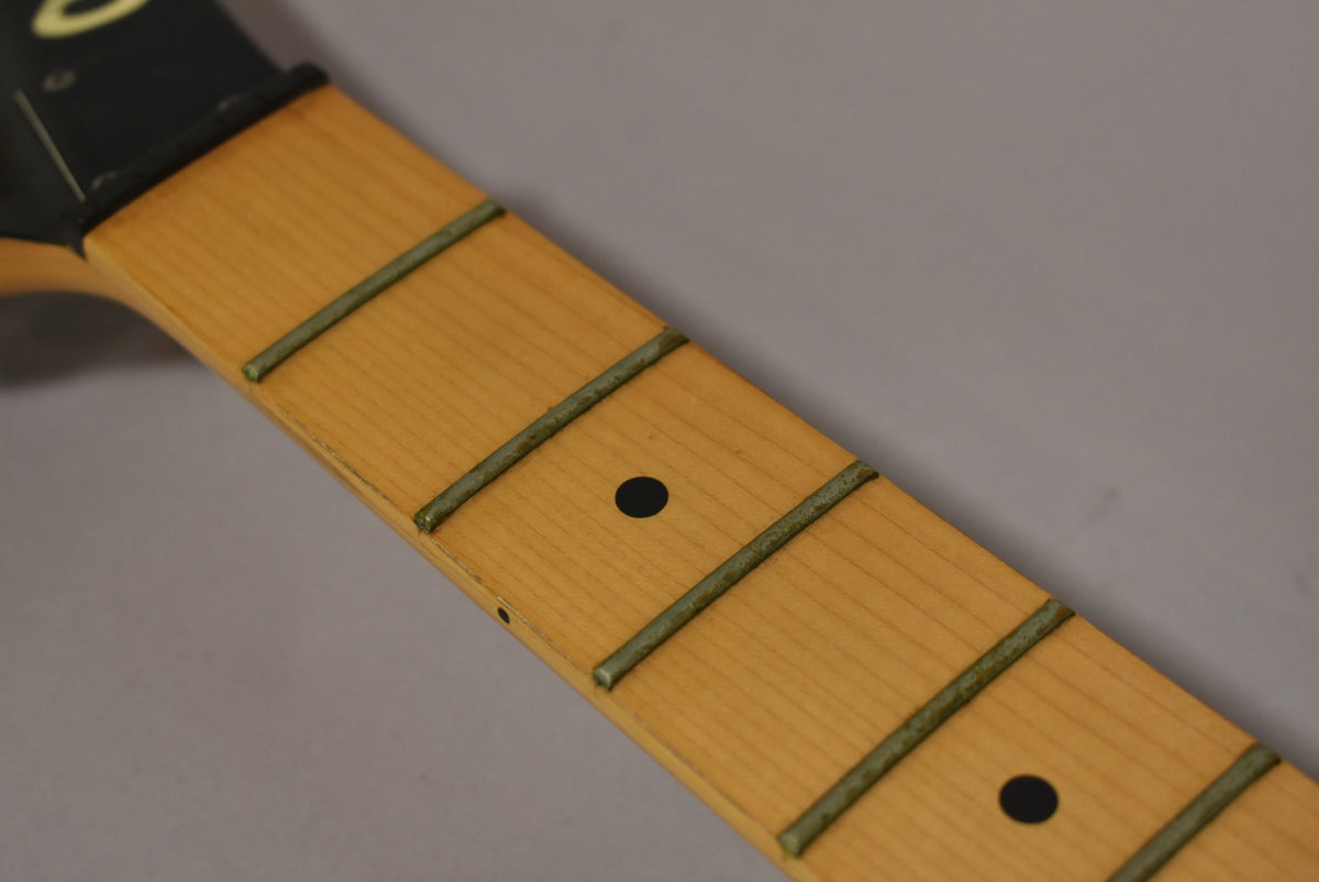 Close-up of the maple fretboard with black dot inlays and tarnished frets, showing wear along the bass side edge.