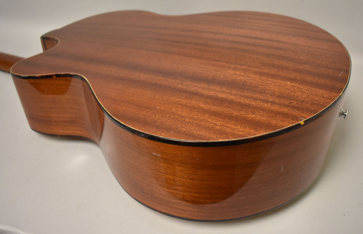 The acoustic bass's natural finish mahogany back and sides show light scratches and a small chip near the endpin.
