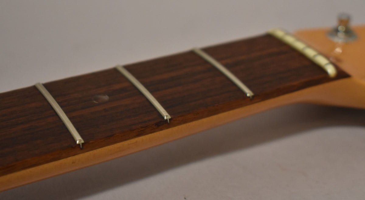 Close-up of the dark rosewood fretboard with light frets and a single dot inlay, showing a light-colored nut and part of a tuning peg.