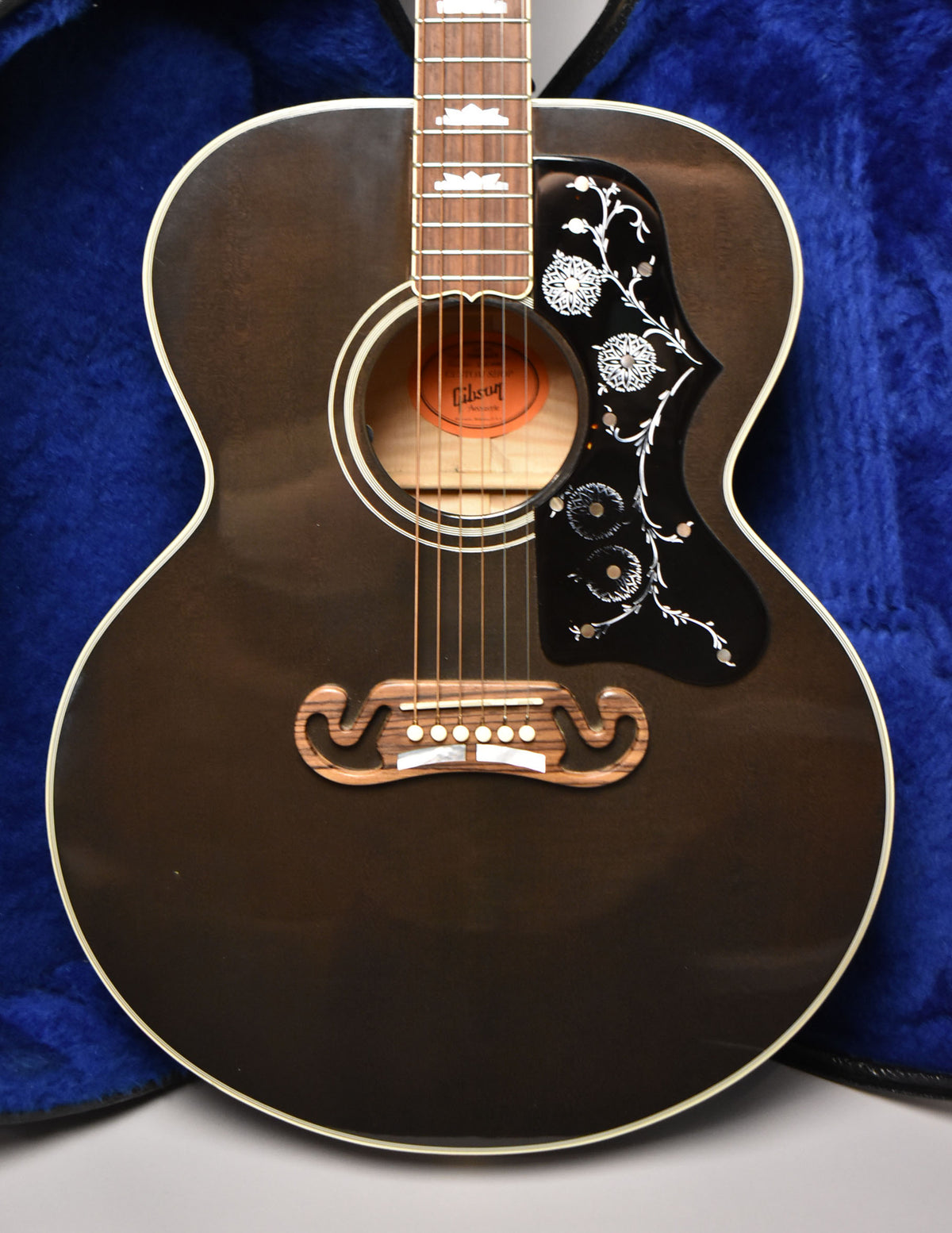 Full-frame, front-facing view of a dark trans black acoustic guitar with a decorative black pickguard and a carved wooden bridge.