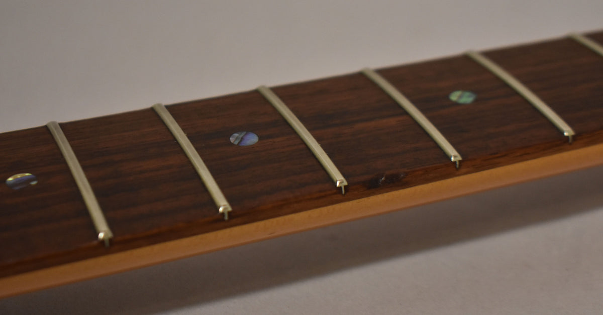 Close-up of the dark rosewood fretboard with five frets and abalone dot inlays, showing some wear and a small ding near the third fret.