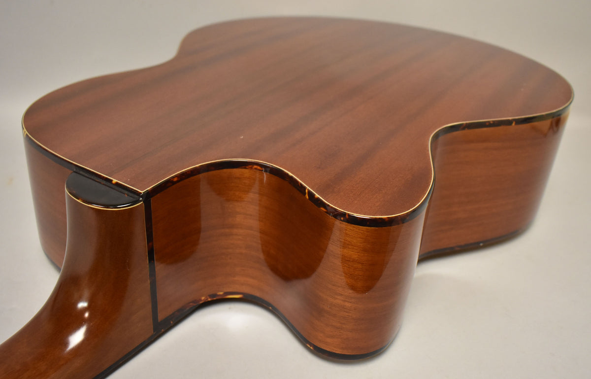 The acoustic bass's natural finish body and neck are shown from the back, with tortoise shell binding and minor wear along the edges.
