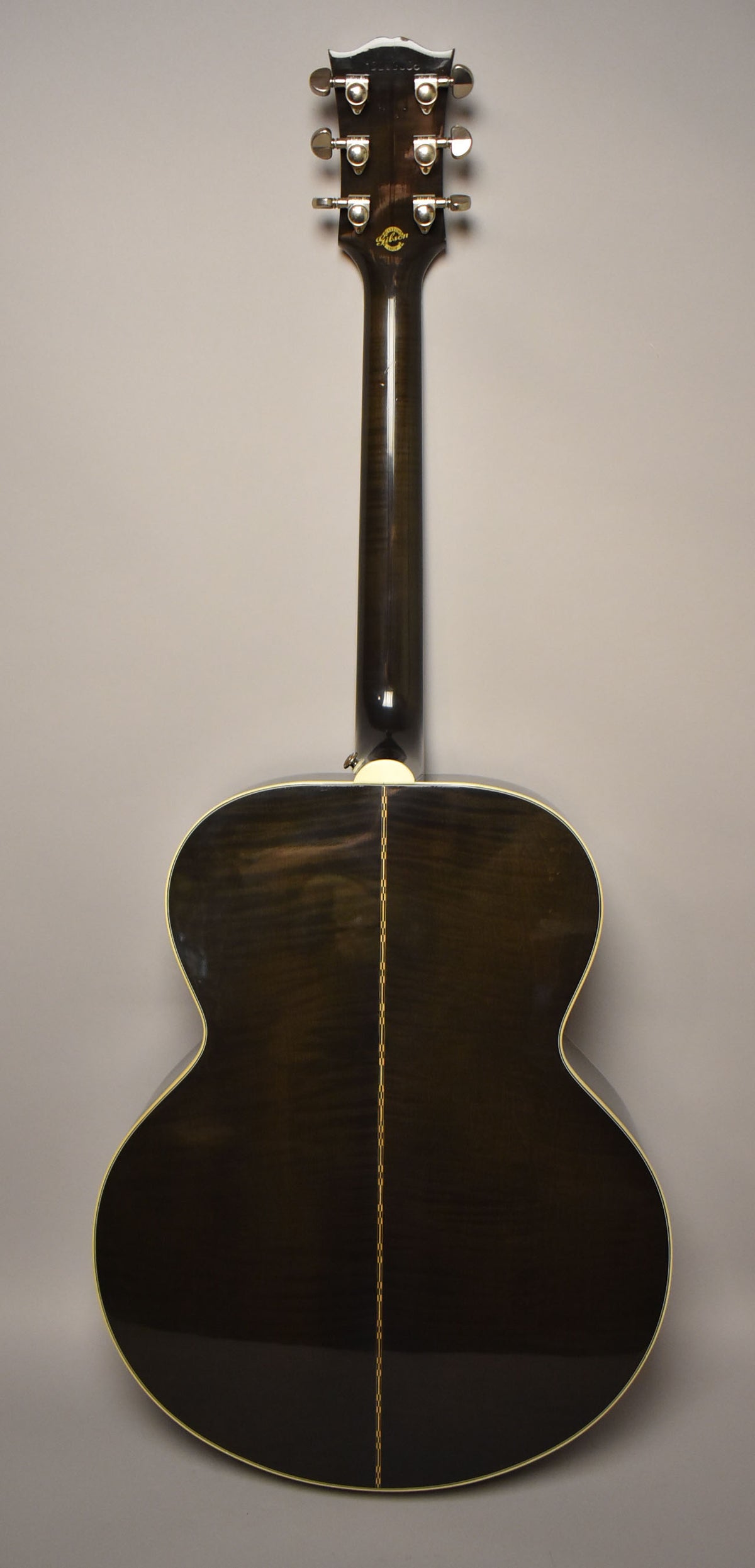 The back of a trans black jumbo acoustic guitar, showing the headstock, neck, and body with a light center stripe.