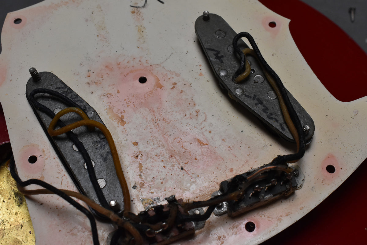 Close-up of the guitar's underside, showing two pickups, wiring, and the back of the pickguard with red paint residue and wear.