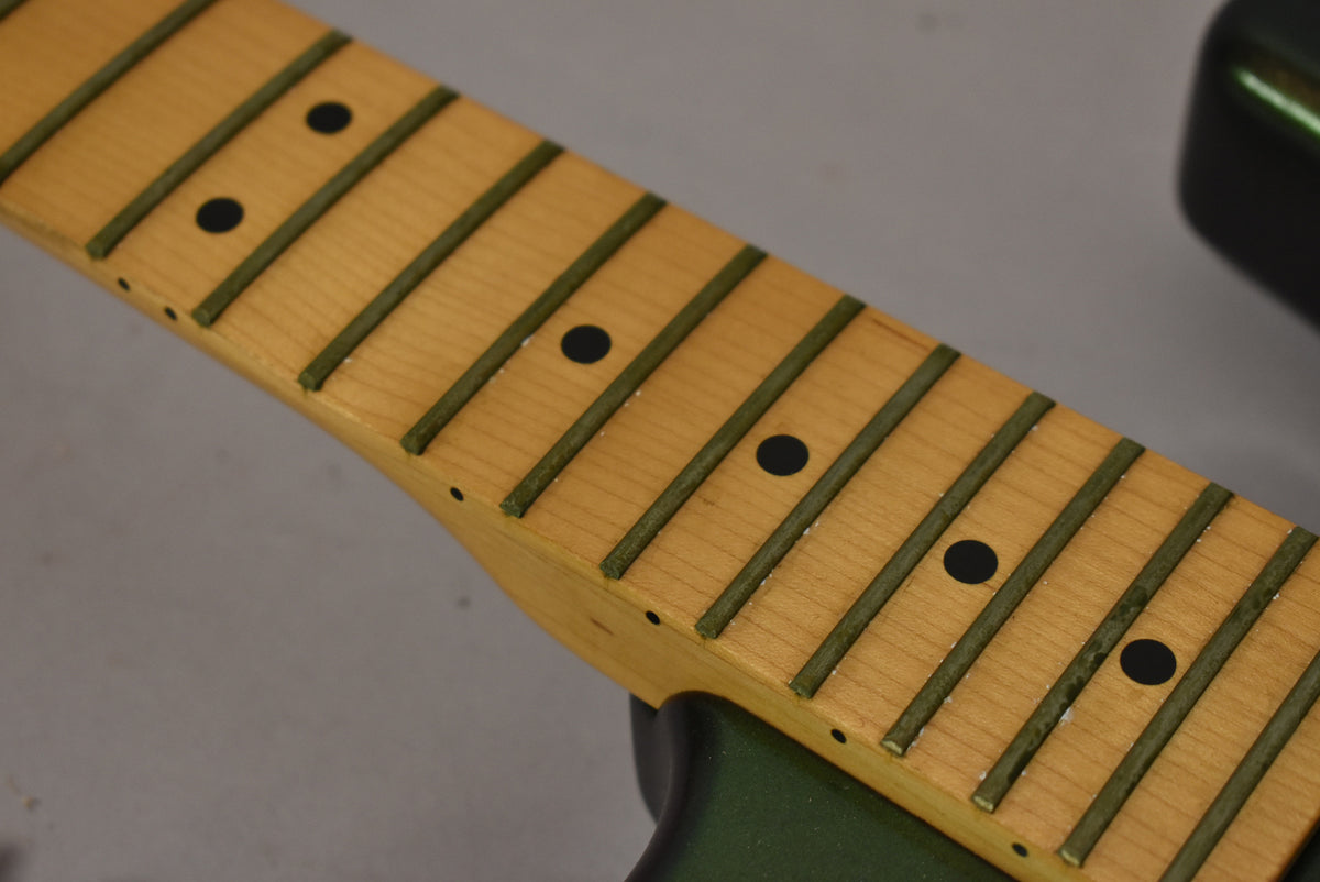 Close-up of the maple fretboard with dark fret markers and green frets, showing wear and white residue on the frets.