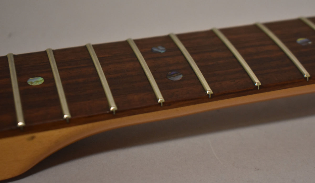 Close-up of a dark rosewood fretboard with abalone dot inlays and light wear on the frets, viewed from the bass side.