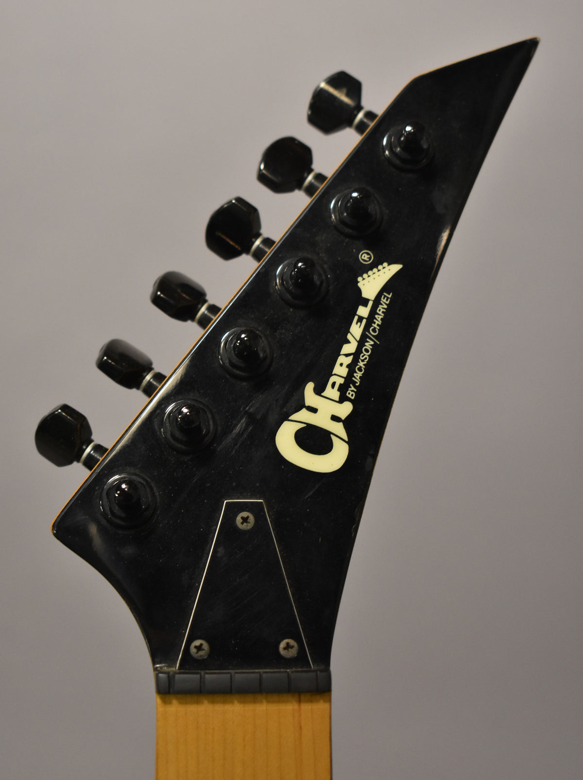 Close-up of the black pointed headstock with six black tuners, a locking nut, and a light maple neck.
