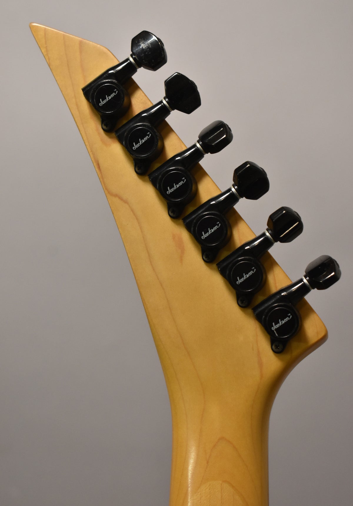 The back of the guitar's natural wood headstock and neck joint, showing six black tuners with visible wear.