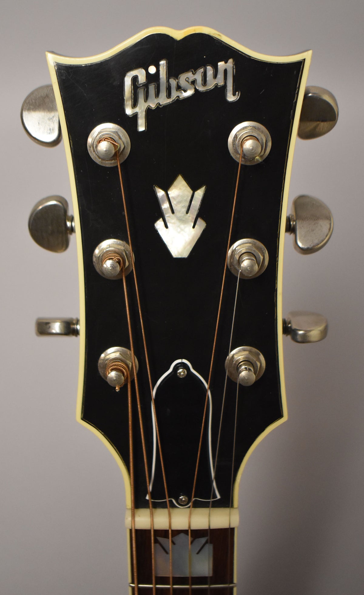 Close-up of the guitar's black headstock with mother-of-pearl inlays, cream binding, and six chrome tuners.