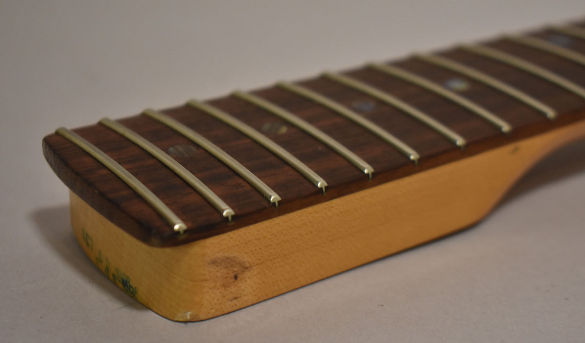 Close-up of the dark rosewood fretboard and light maple neck heel, showing some wear and a green sticker on the side.