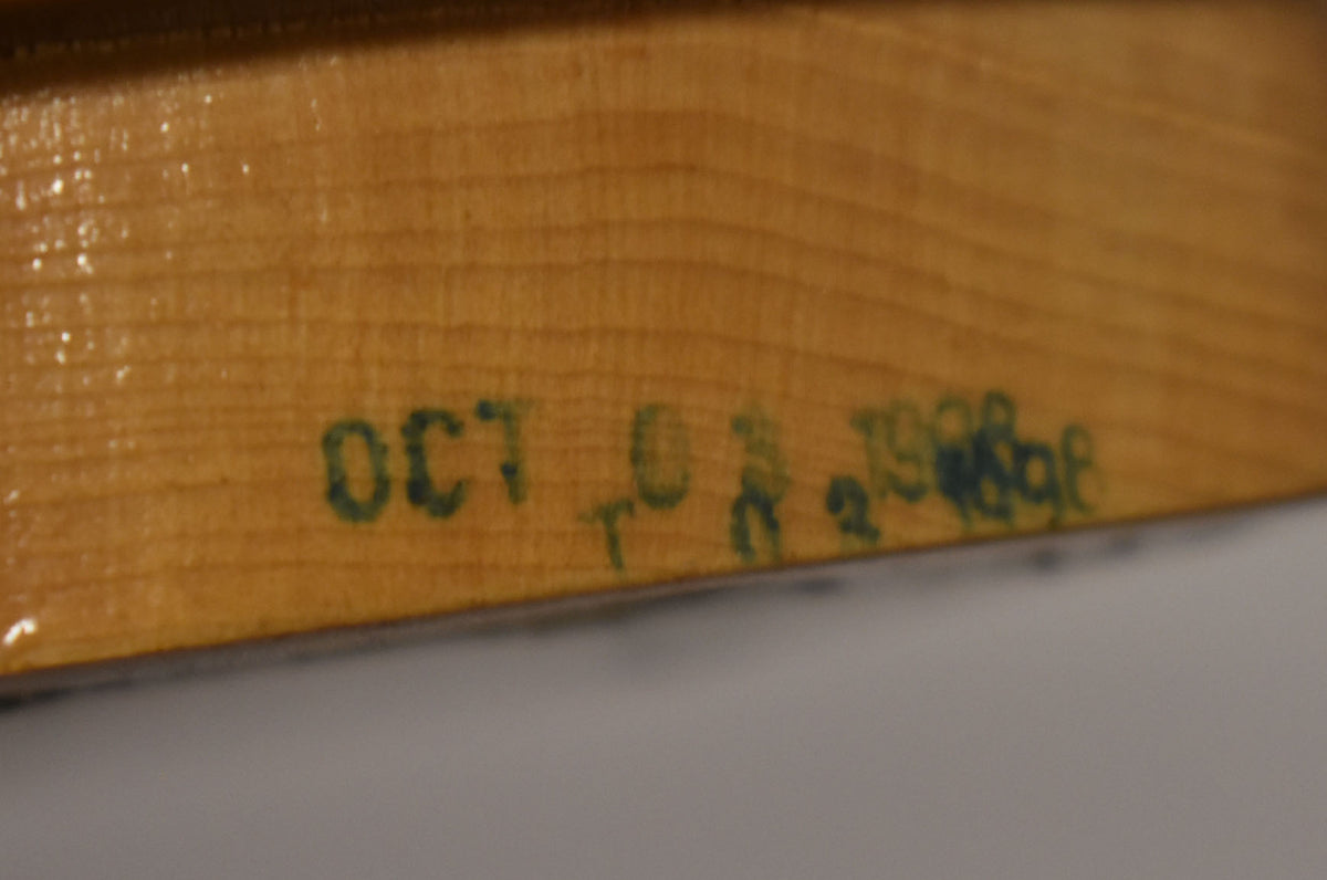 Close-up of the neck heel, showing a light wood grain with a faint green "OCT 02 1998" stamp.