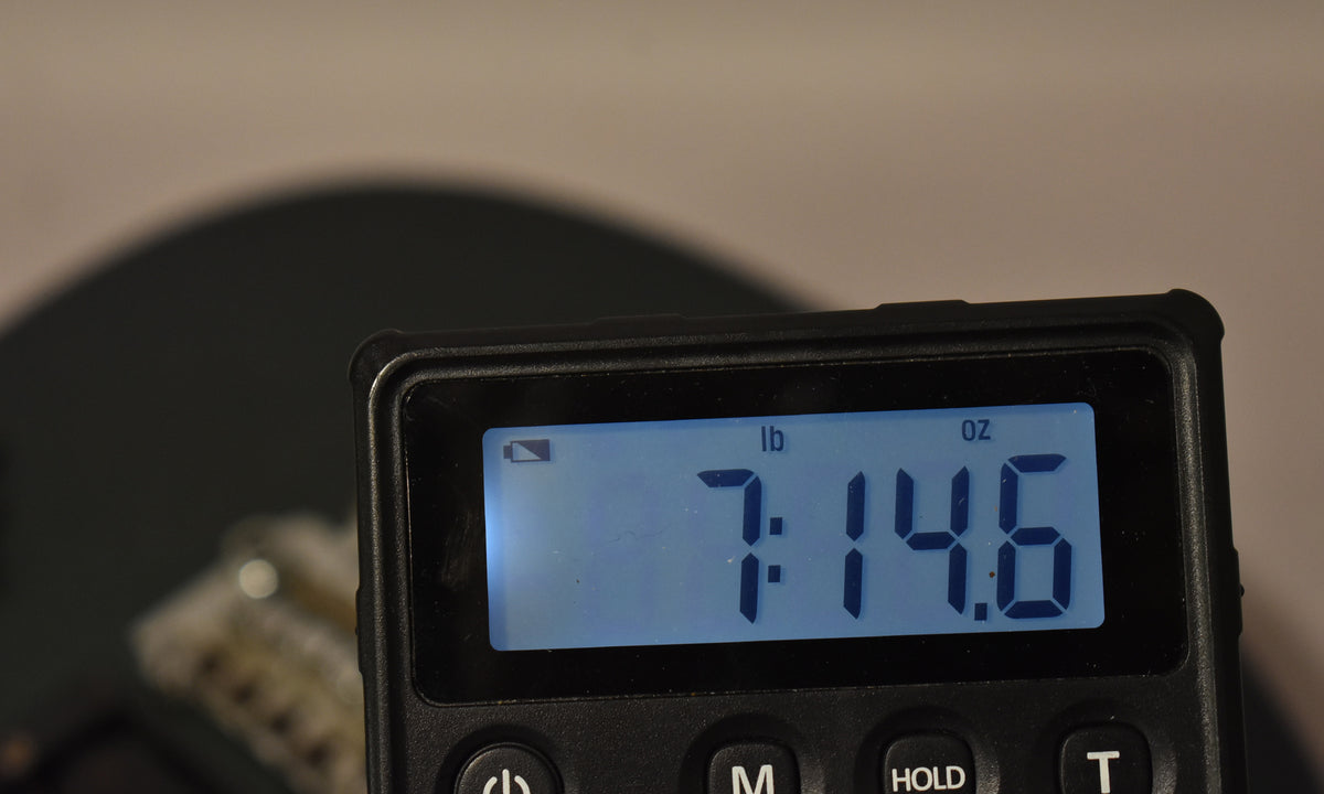 A digital scale displays the guitar's weight as 7 pounds, 14.6 ounces, with a blurred dark guitar body in the background.