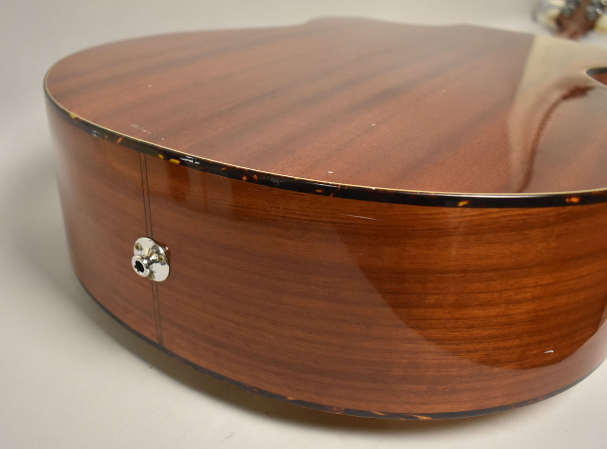 Close-up of the acoustic bass's lower bout, showing the glossy natural finish, tortoise shell binding, and a chrome endpin jack.