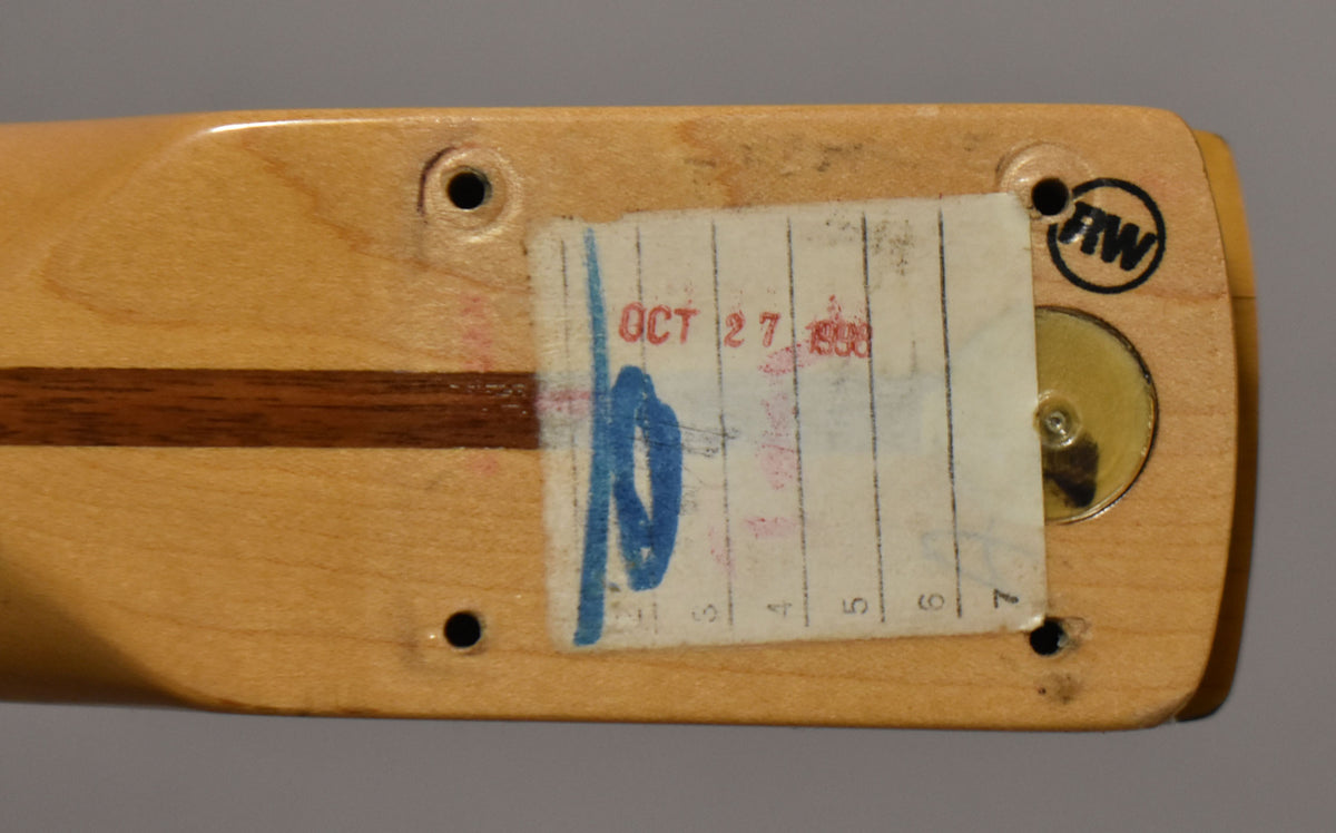 The maple neck heel, with a dark walnut skunk stripe, shows a worn paper label and four screw holes.