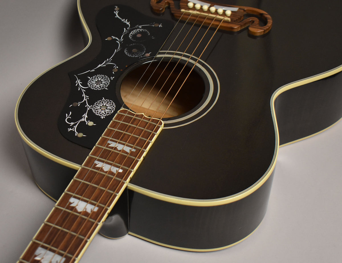 The upper body of a black acoustic guitar, showing a decorative pickguard and ornate mother-of-pearl fretboard inlays.