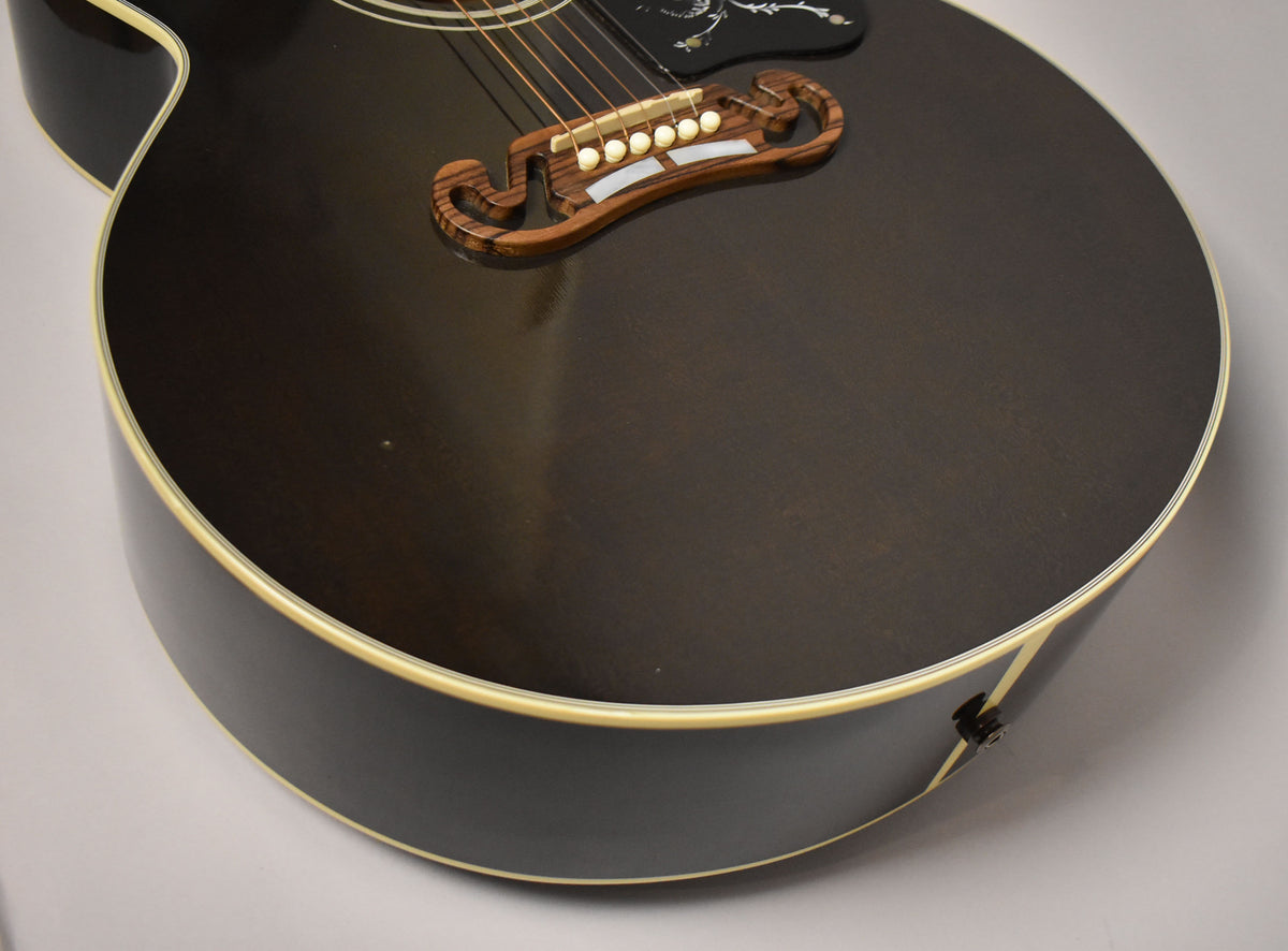 Upper right view of the guitar's body, showing the dark trans black finish, ornate wooden bridge, and a few small dings on the top.