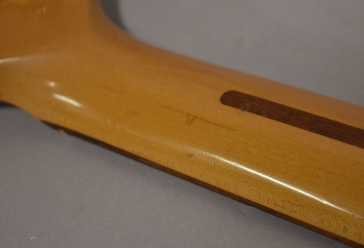 The back of a light amber guitar neck, showing a dark brown skunk stripe and minor surface scratches.