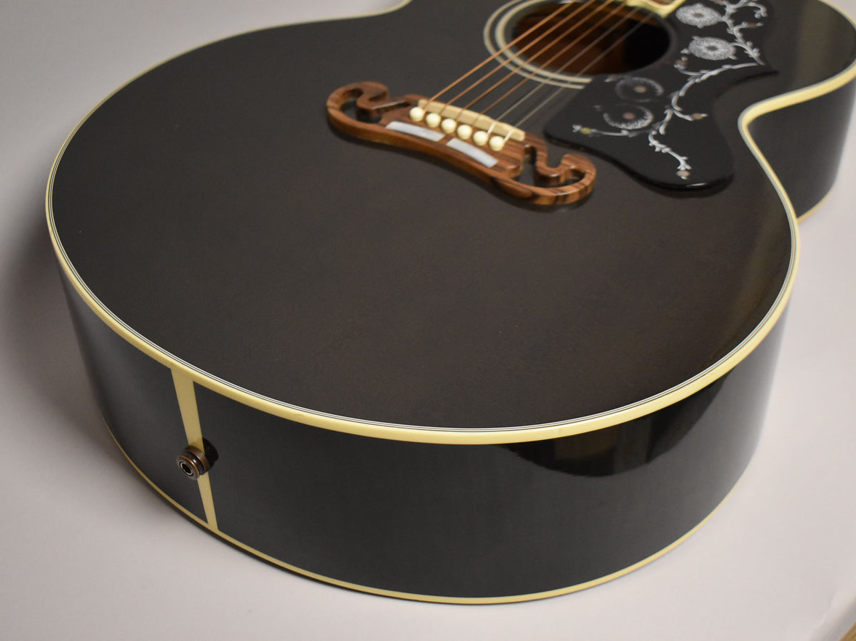The black acoustic guitar's lower bout and side are angled, showing the ornate bridge, pickguard, and endpin jack.