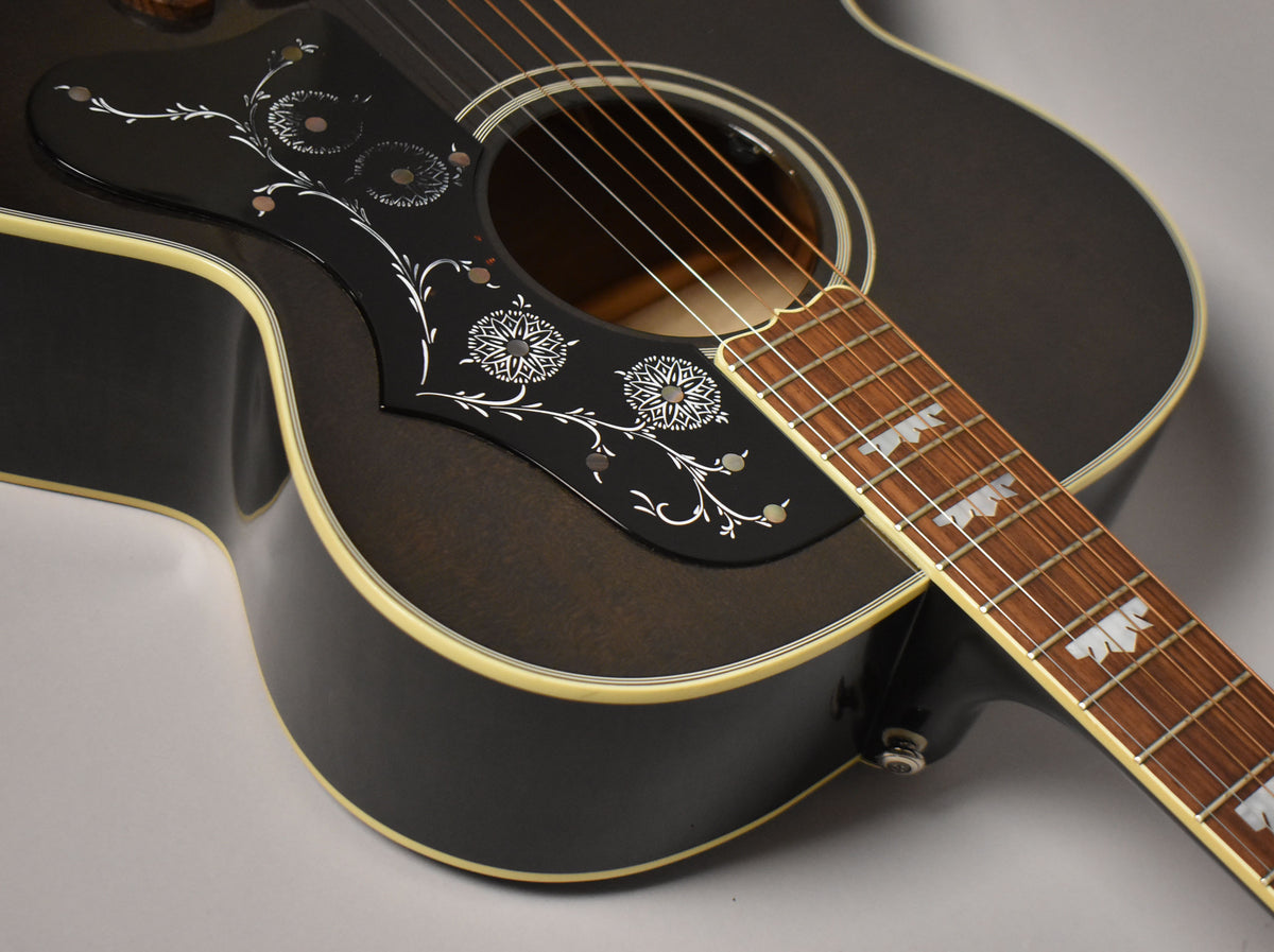 The upper body of a black acoustic guitar with a decorative pickguard and leaf-shaped fretboard inlays.