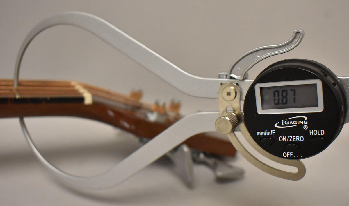 A digital caliper measures the neck thickness at the first fret, displaying "0.87" on its screen.