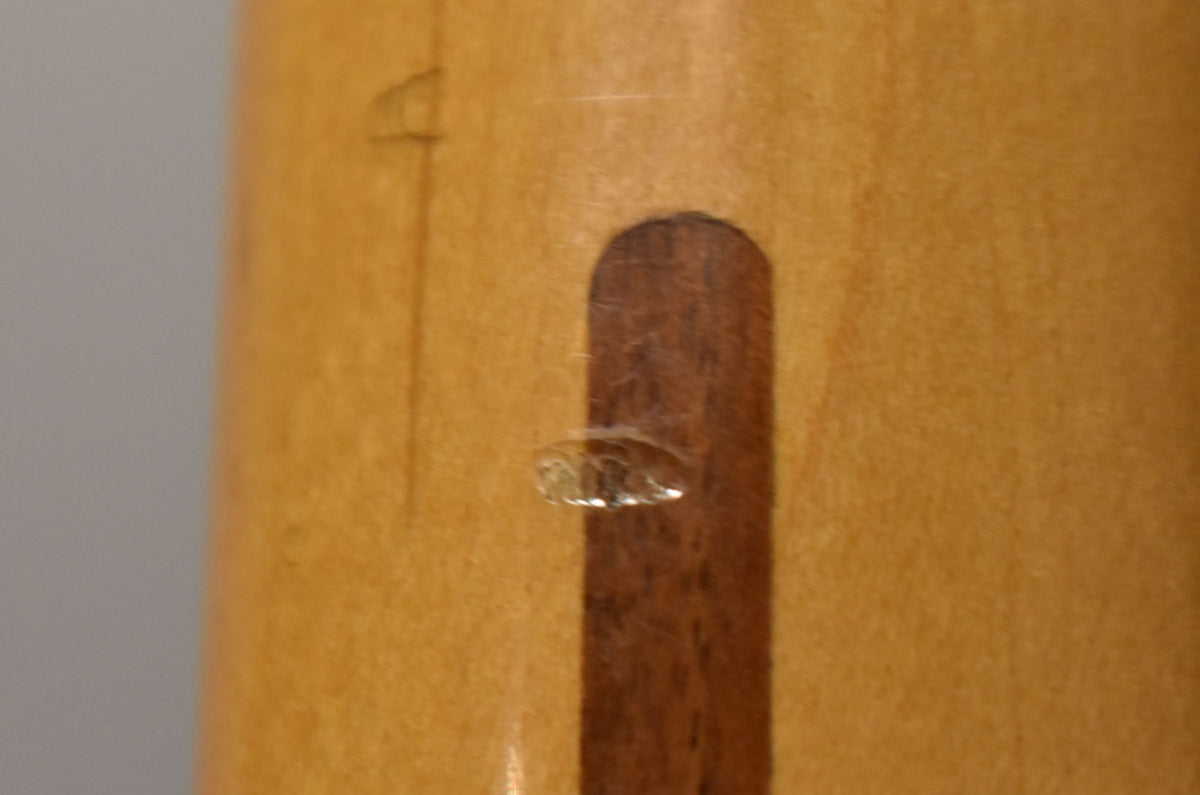 Close-up of the neck's back, showing a dark wood skunk stripe, a small chip in the finish, and light wear on the maple.