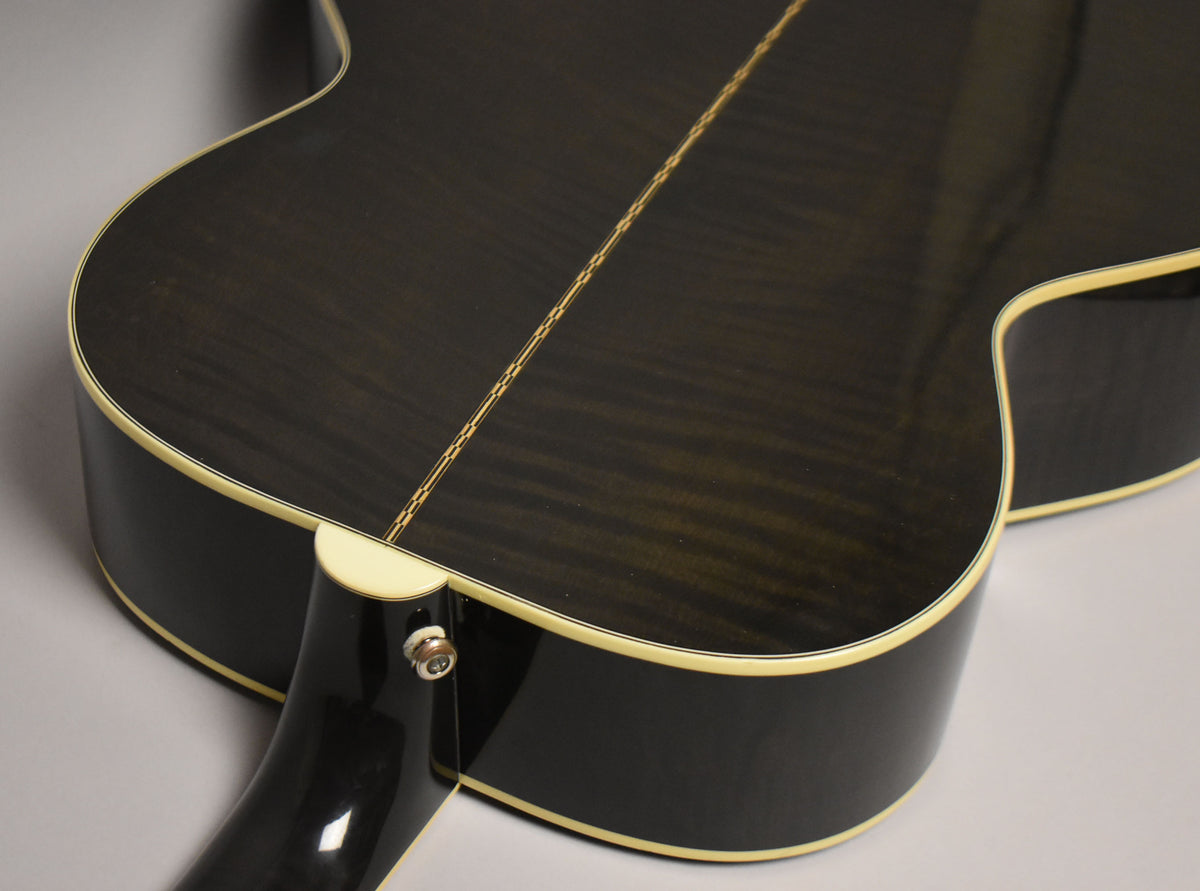 The back of a black acoustic guitar, showing the dark wood grain, cream binding, and a chrome endpin jack.