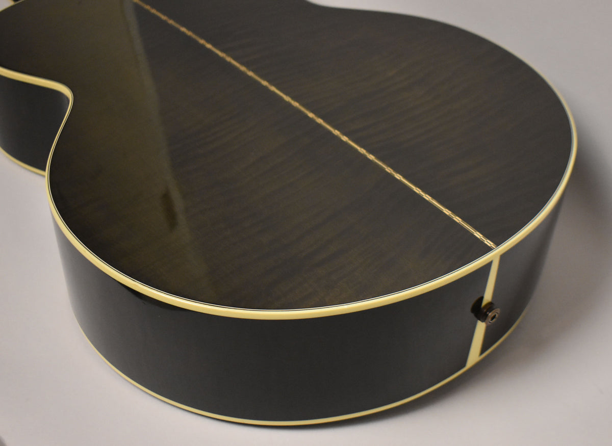 The lower bout of a trans black acoustic guitar, showing the figured wood grain and cream binding, with an endpin jack.