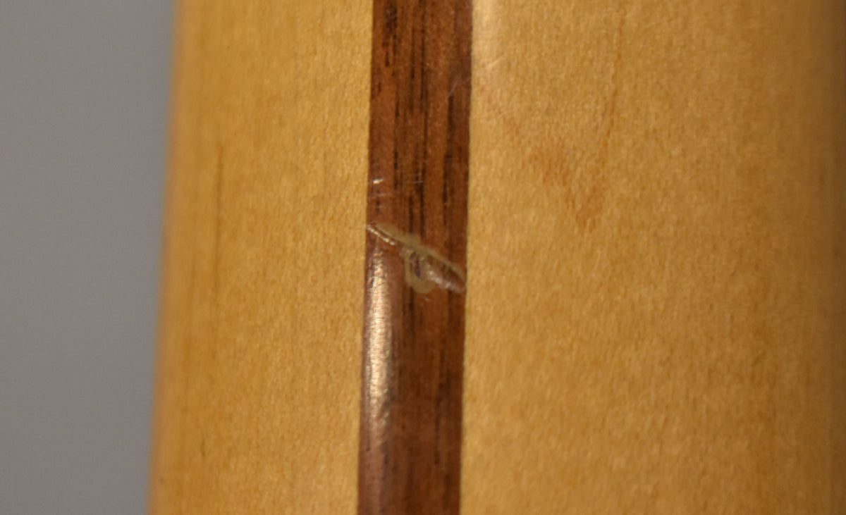 Close-up of the neck's back, showing a dark wood stripe with a visible scratch and light wood on either side.