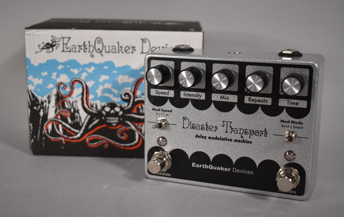 A silver glitter-finish delay pedal with five black-knobbed controls, two toggle switches, and two footswitches, shown with its box.
