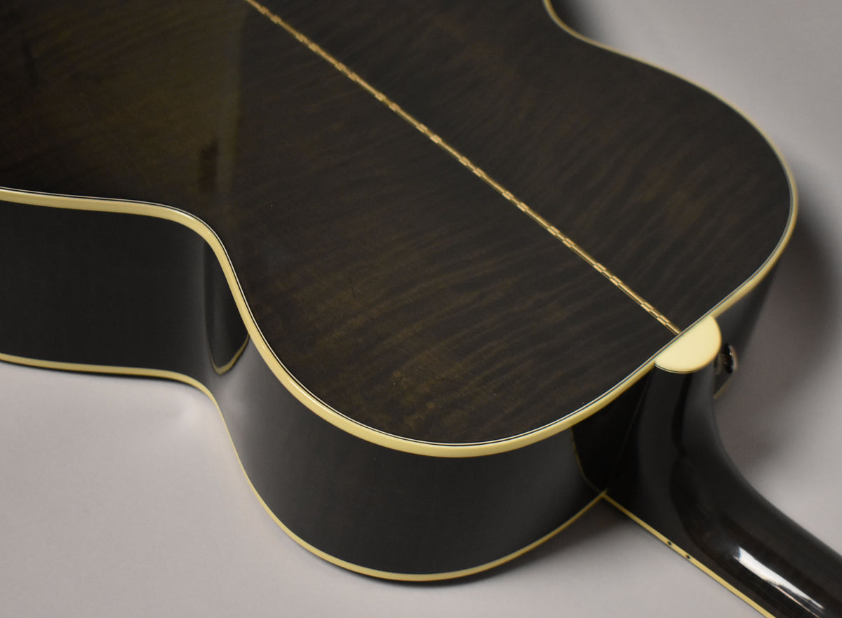 The guitar's dark trans black back and sides show subtle wood grain, with cream binding and a visible endpin jack.