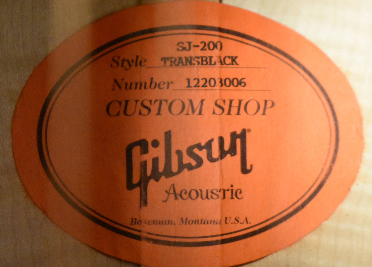 A close-up of the guitar's orange oval soundhole label, showing "SJ-200," "TRANSBLACK," and "CUSTOM SHOP" in black text.